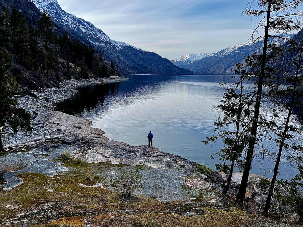 A lone figure on a granite point above still water, with snow-dusted peaks closing the end of the lake