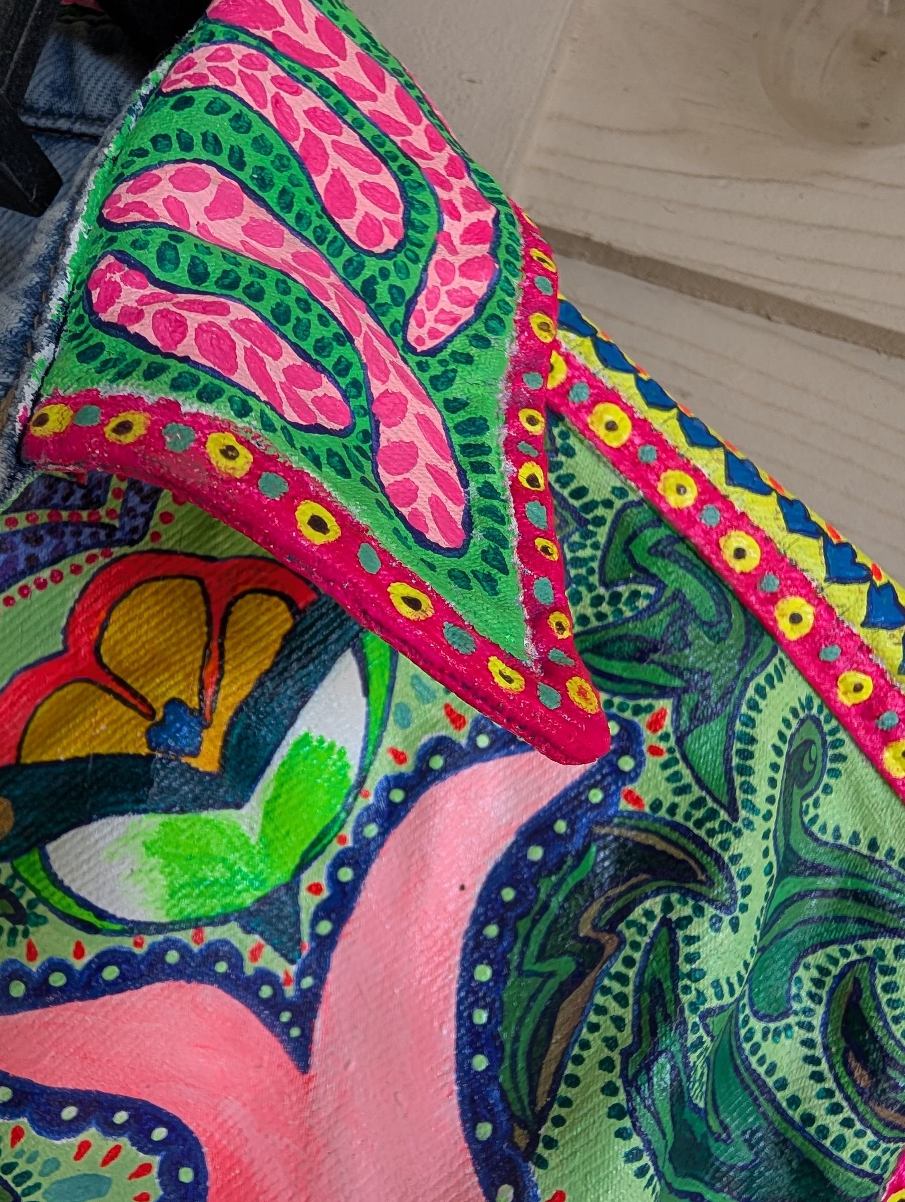 Close view of a hand-painted denim collar with pink and green paisley patterns.