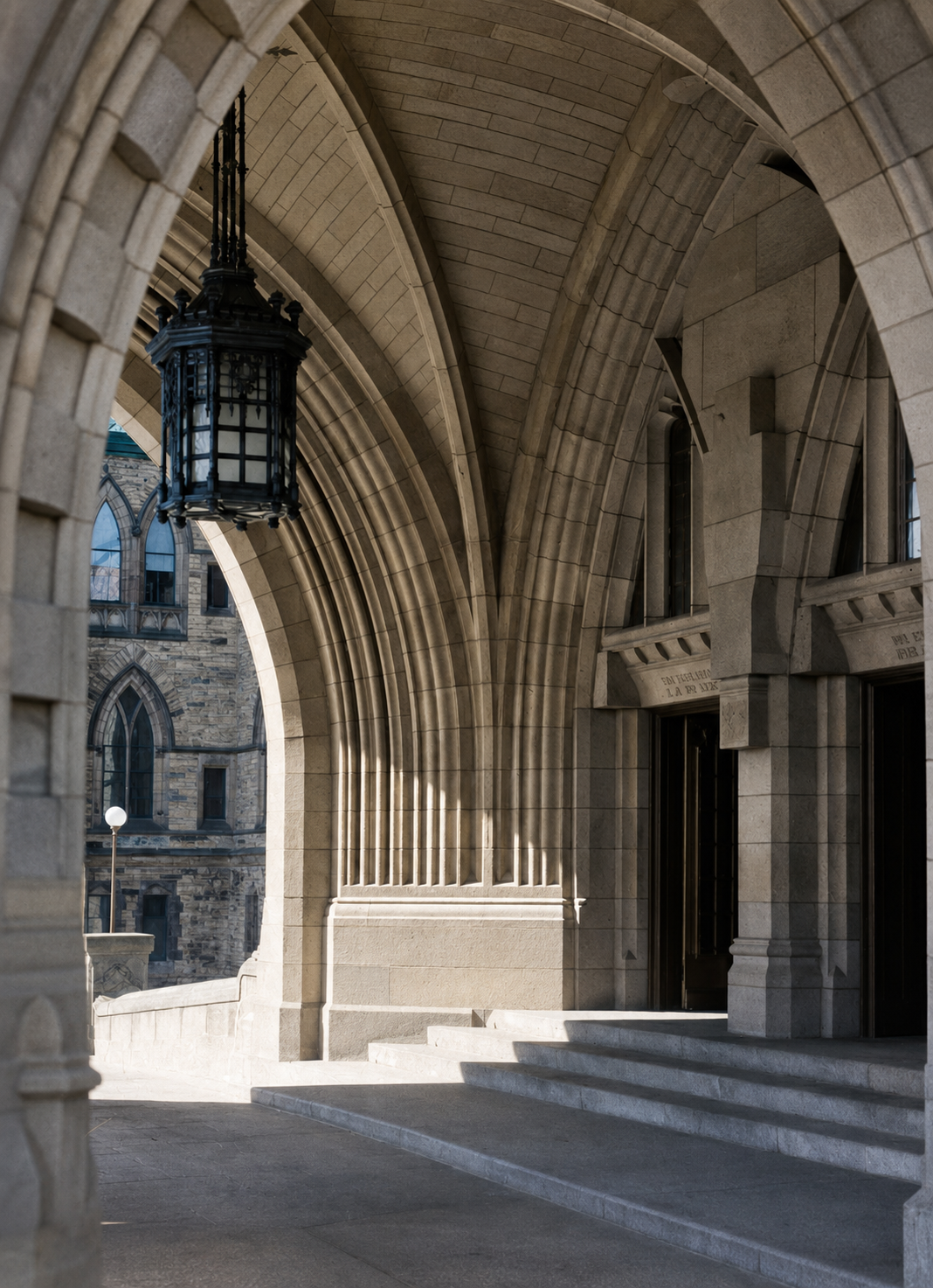 An empty stone arcade beneath the Peace Tower of the Parliament Buildings in Ottawa, photographed in 1934, with sunlight falling across the steps.
