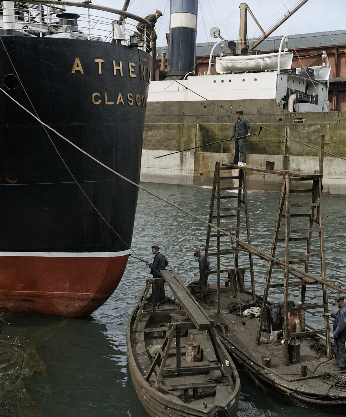 The stern of the liner Athenia at a Glasgow dock, her name and port of registry visible, with workers on wooden barges alongside.