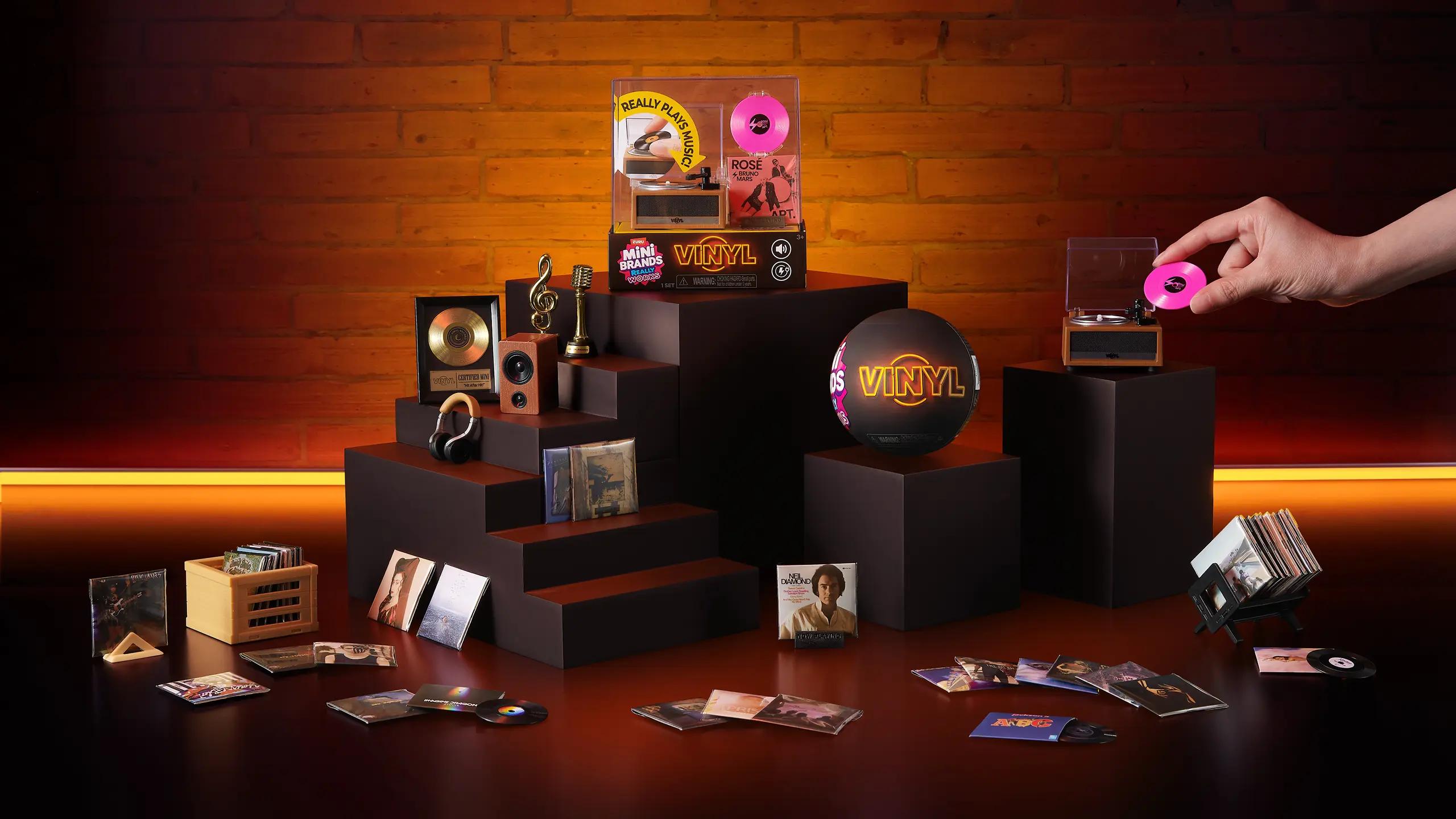 Interactive setup of ZURU Mini Brands Sneakers collection with a hand placing a miniature sneaker on a pedestal, surrounded by sports-themed items including tennis balls, a water bottle, a cap, and a racket on a blue background.