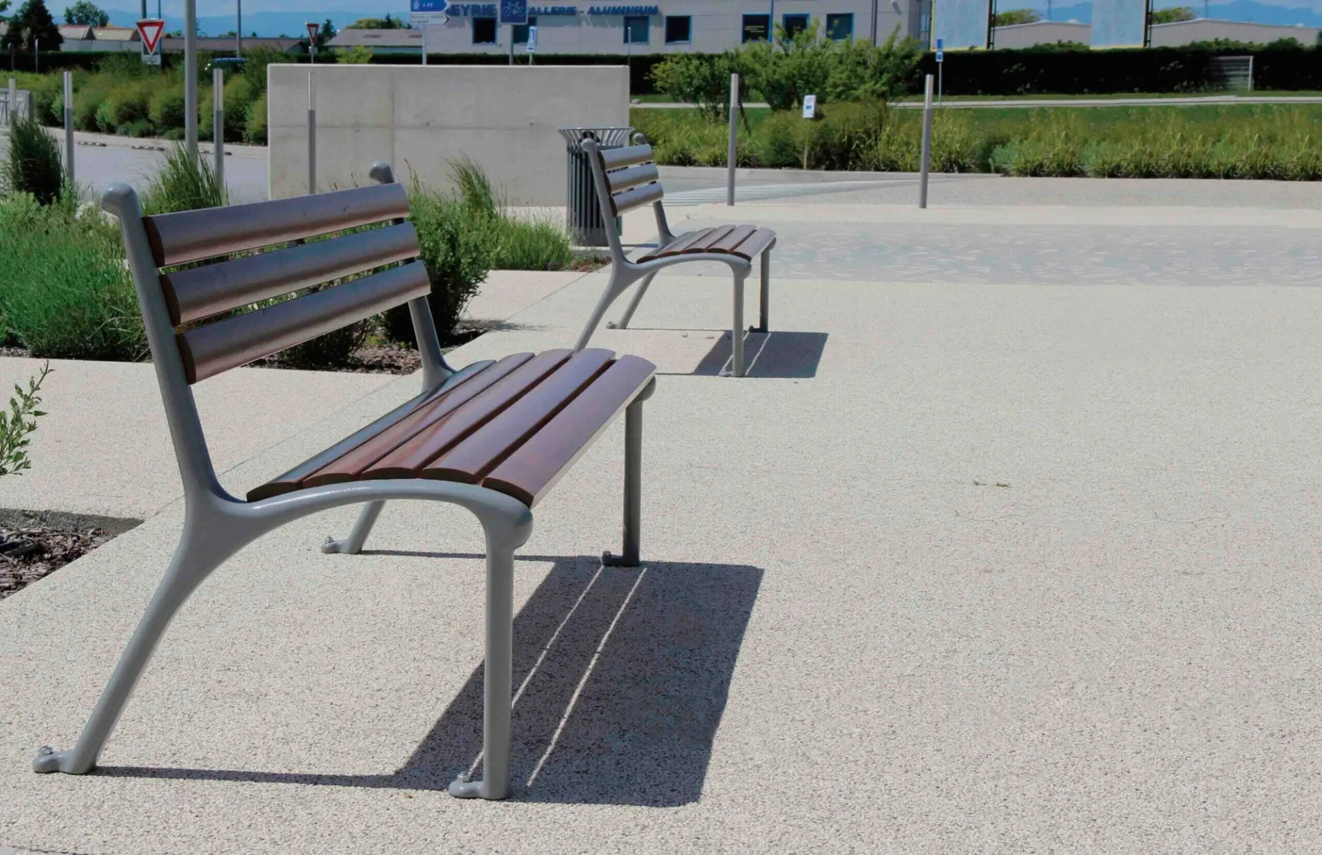 Two park benches with wooden slats and grey cast frames on a paved plaza