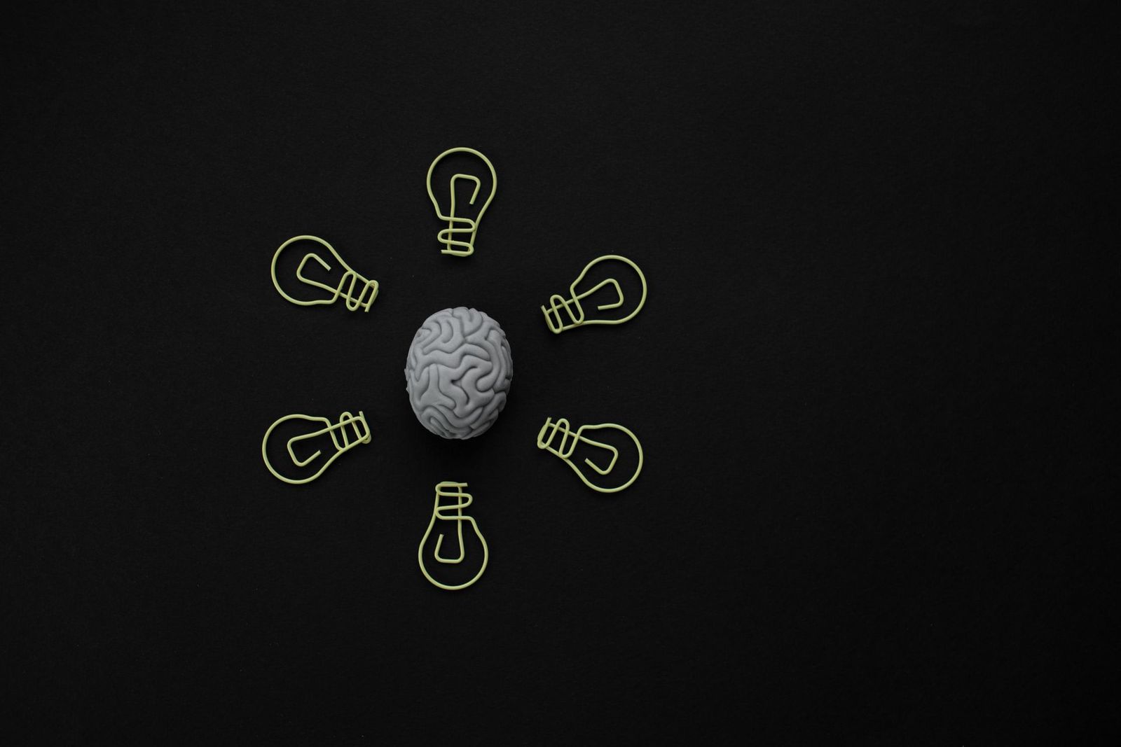 Una figura de cerebro rodeada de clips con forma de bombilla sobre fondo negro.