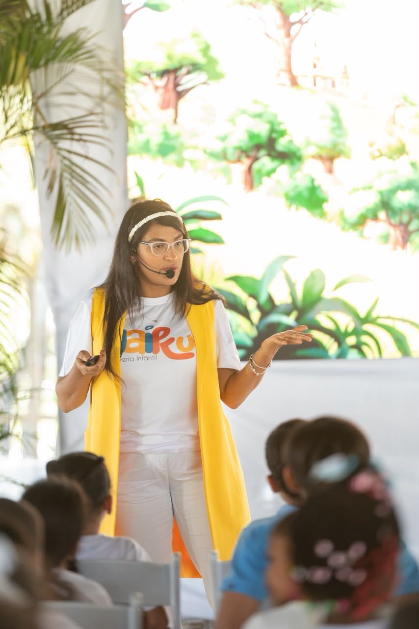 La cuentacuentos, con chaleco amarillo, habla con las niñas y los niños.