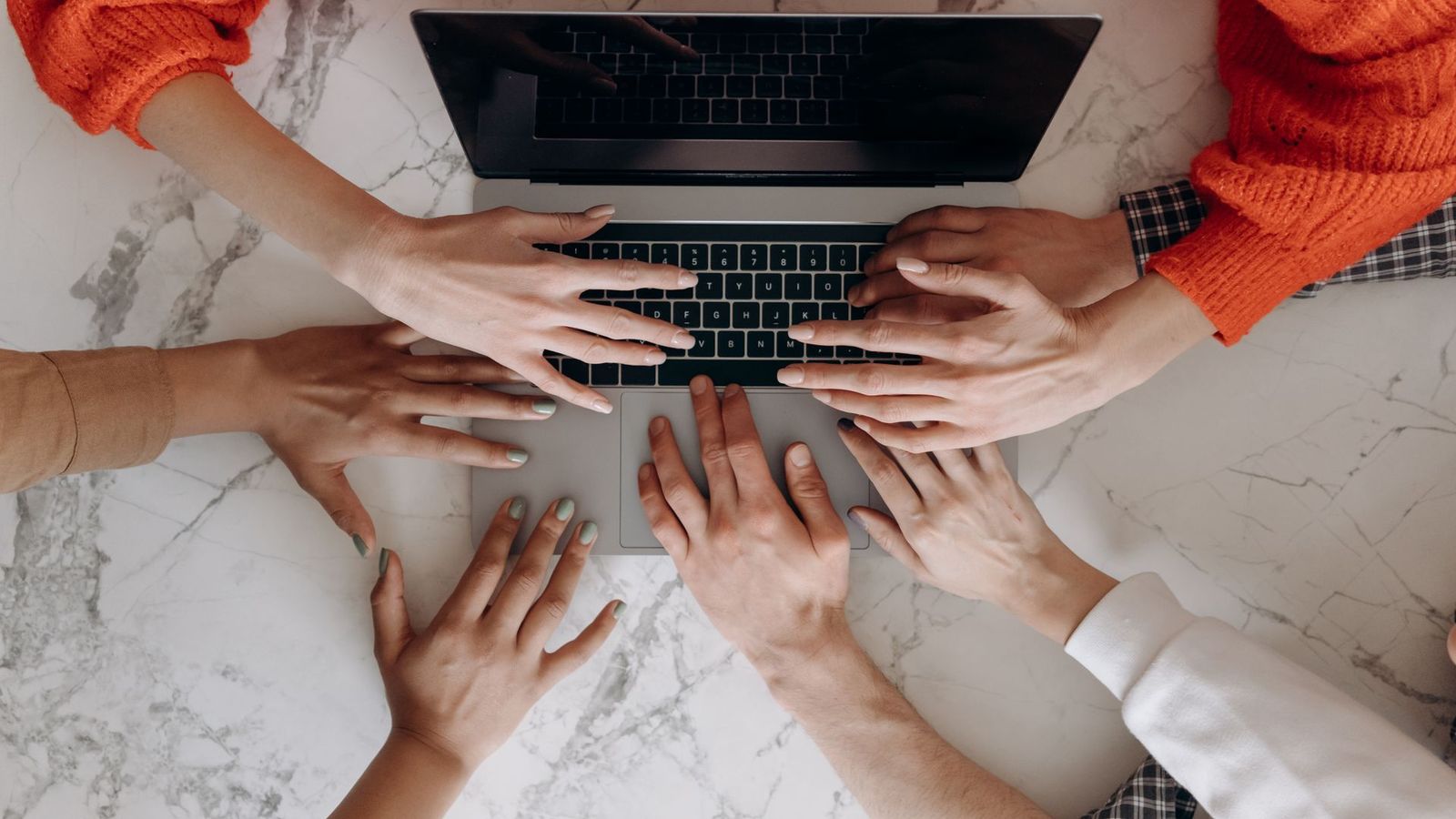 Varias manos de distintas personas sobre el teclado de un mismo portátil.