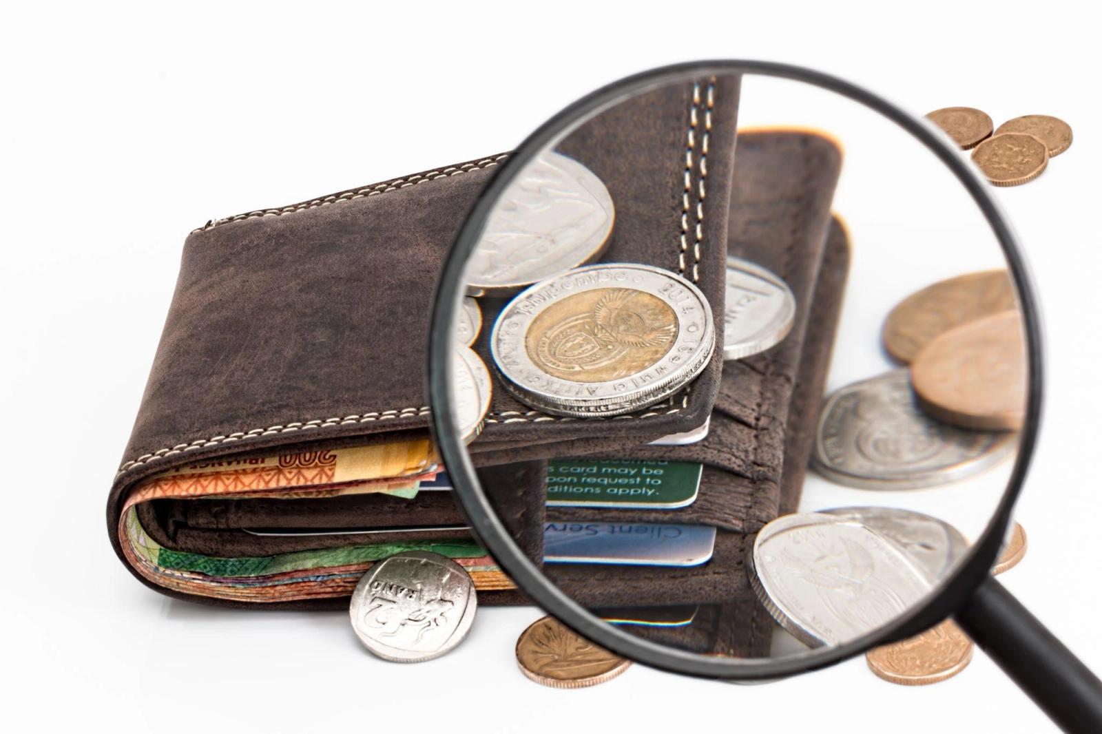 Una cartera de cuero con billetes, tarjetas y monedas, vista a través de una lupa.