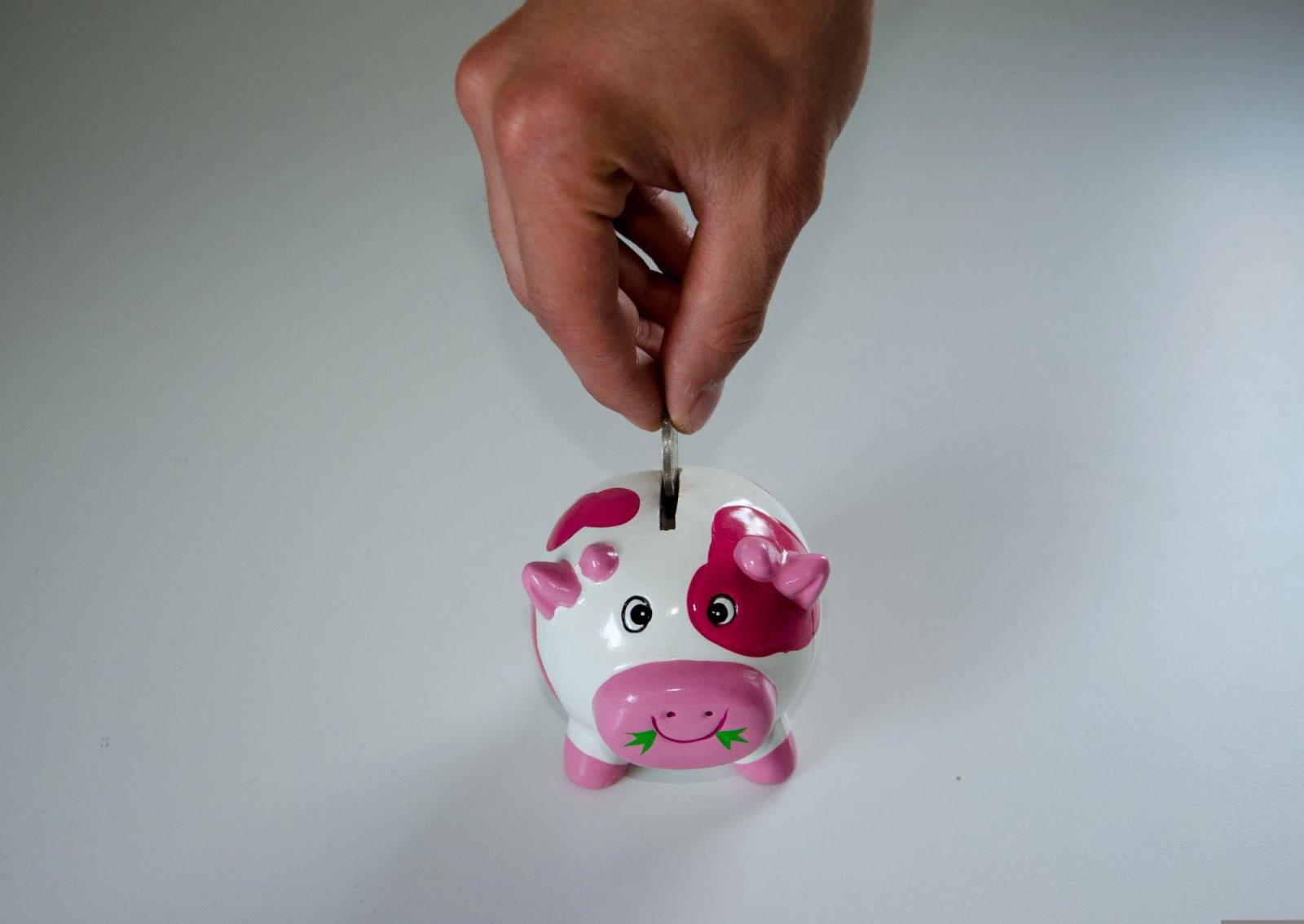 Una mano echa una moneda en una alcancía de cerámica.