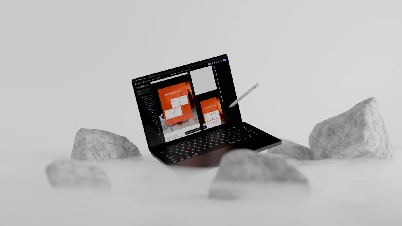 A laptop and stylus among white rocks in fog, its screen showing orange web page layouts in a design tool