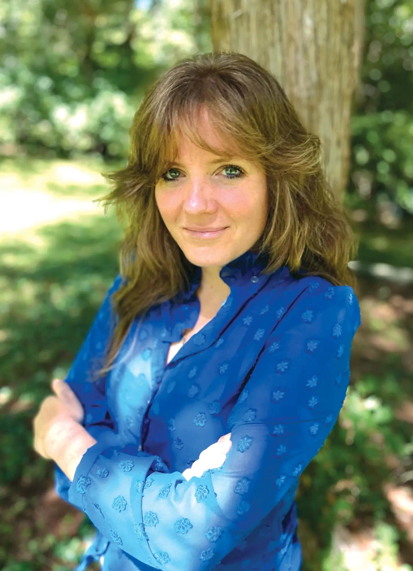 Illustrator Susanna Chapman posing with her arms crossed next to a tree