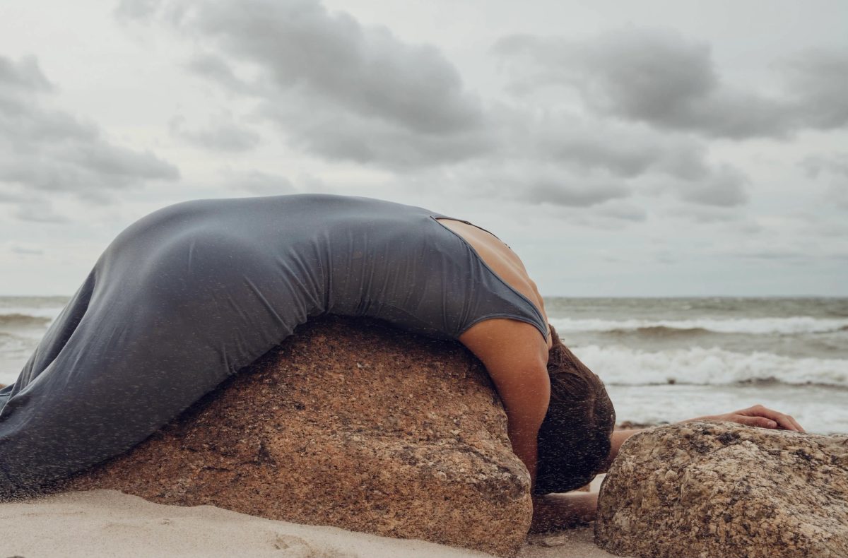 Isabelle draped backwards over a rock by the sea