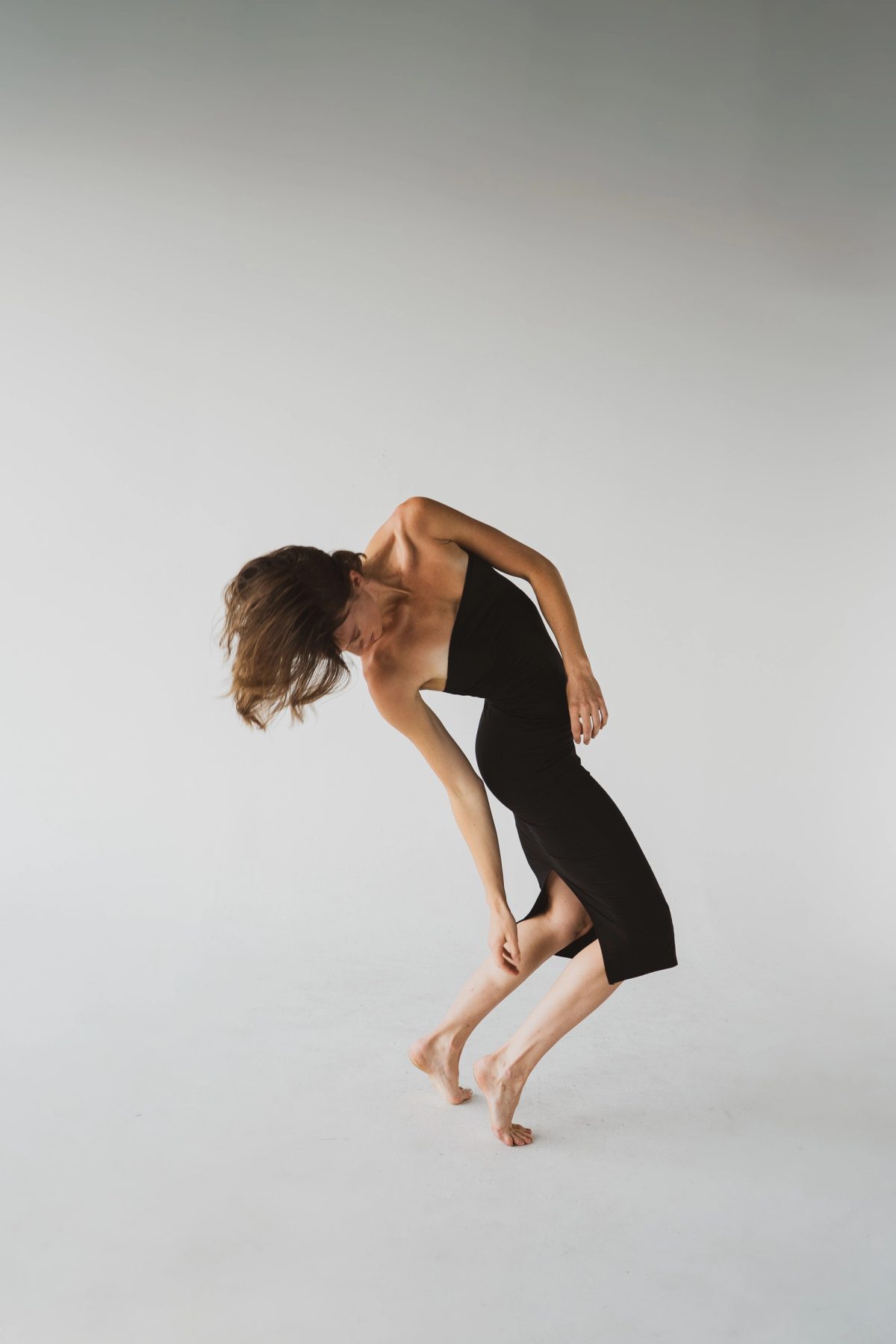 Isabelle in a black dress, folded forward, one knee lifted