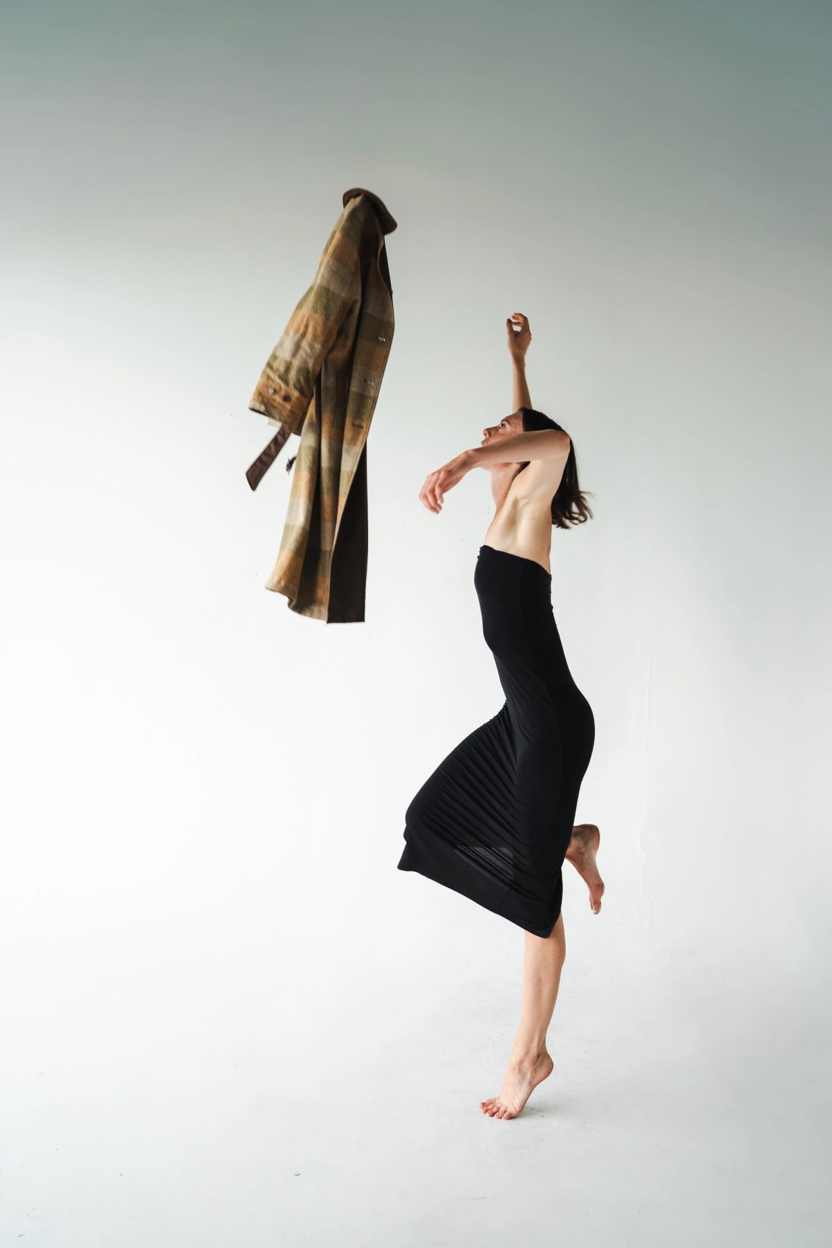 Isabelle in a black dress beside a coat suspended in midair