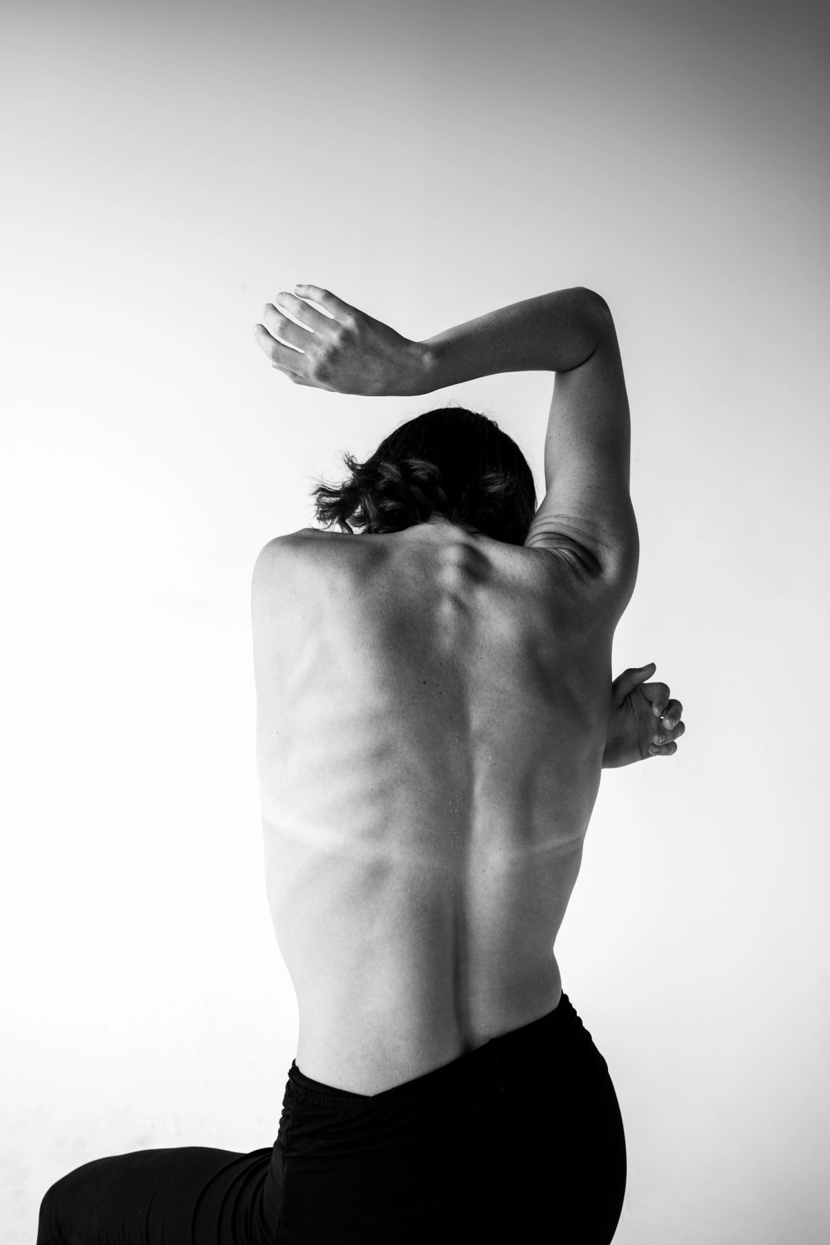 Black and white photo of Isabelle’s bare back, arms crossed over her head