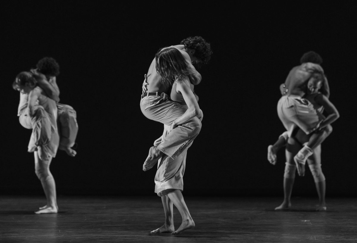 Three pairs of dancers on a dark stage, each carrying a partner