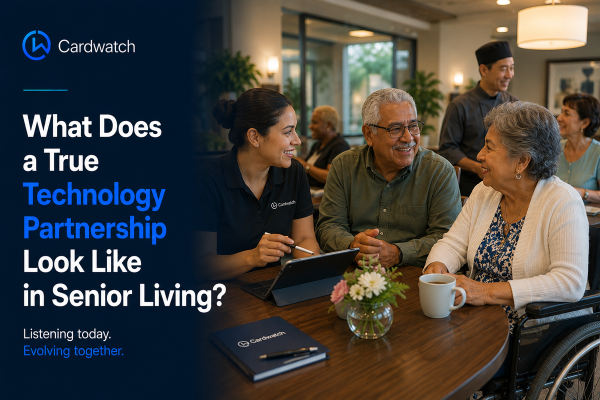 A Cardwatch team member talks with two senior residents over coffee in a community dining room while a chef works in the background.
