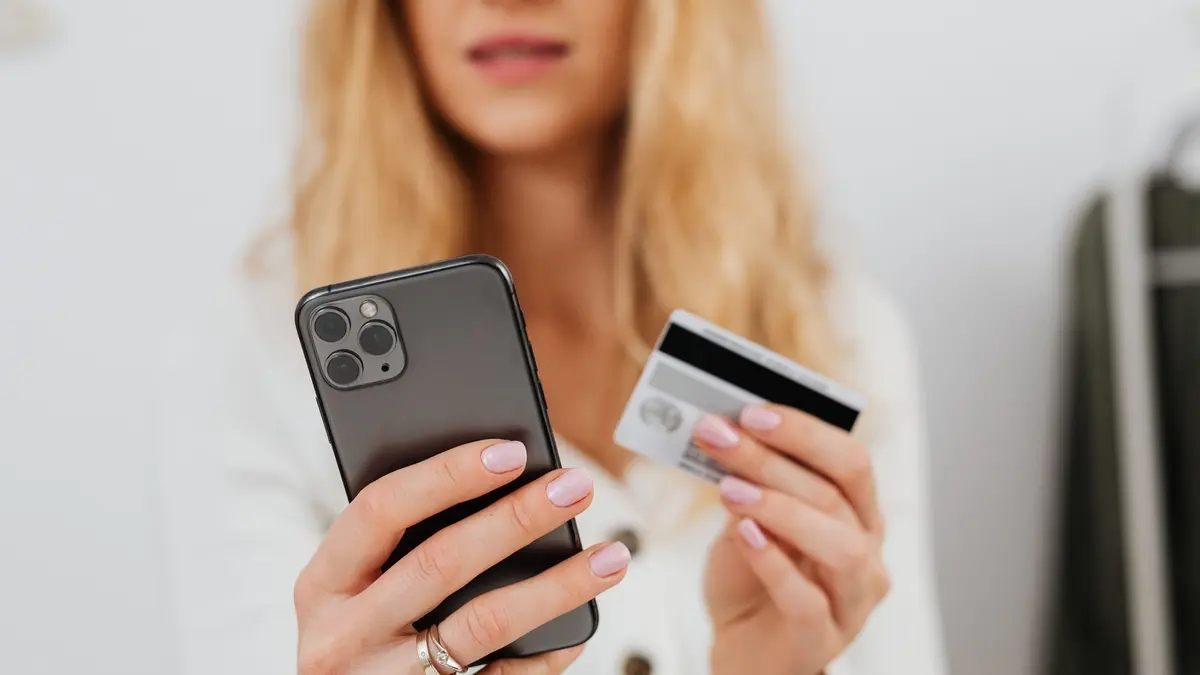 A shopper holding a smartphone in one hand and a bank card in the other while buying online