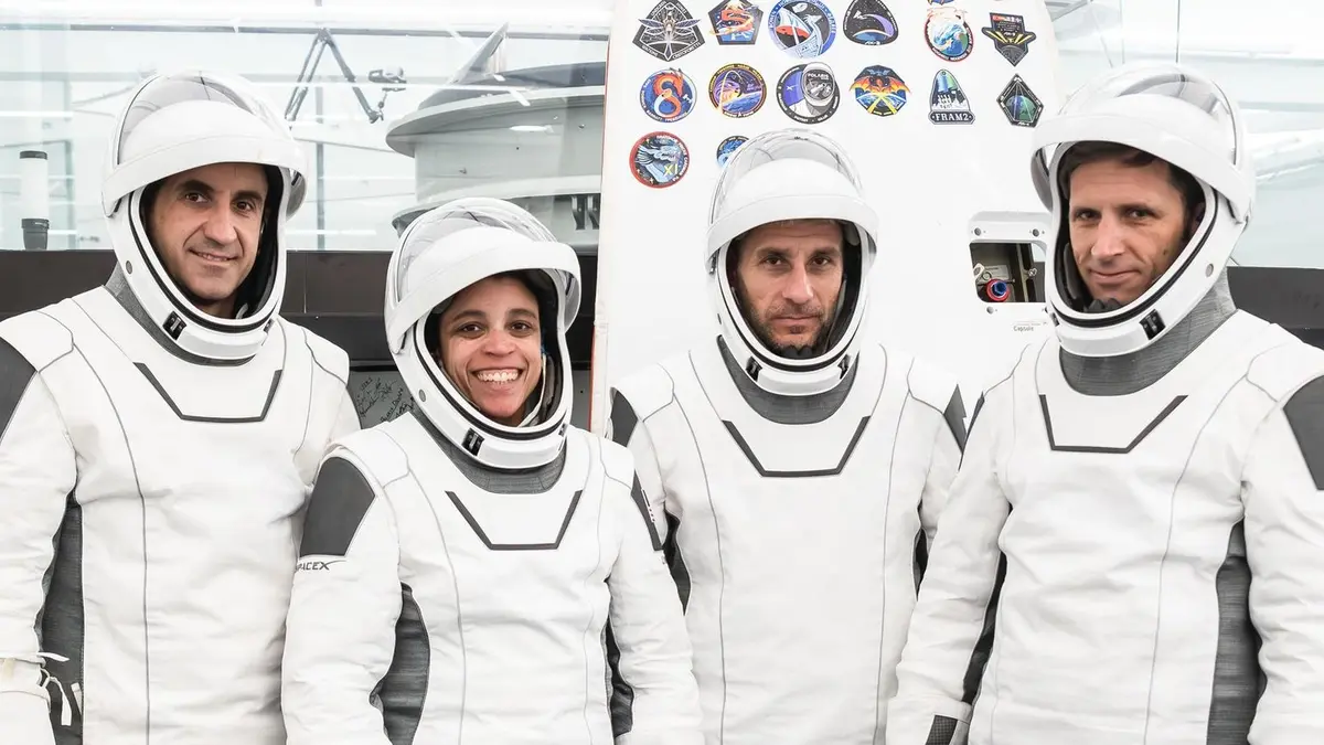 The four Crew-13 astronauts in white SpaceX pressure suits, posing together in front of a wall of mission patches