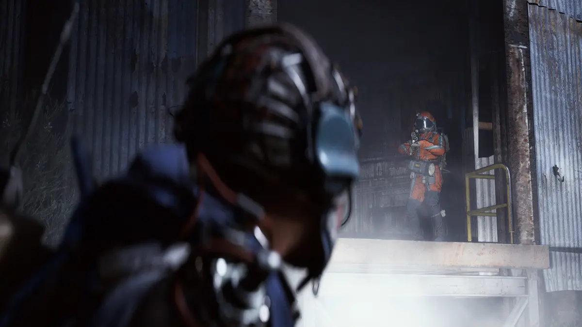 A masked ARC Raiders character in a respirator and rig watches a second raider in an orange suit covering a doorway inside a rusting industrial building