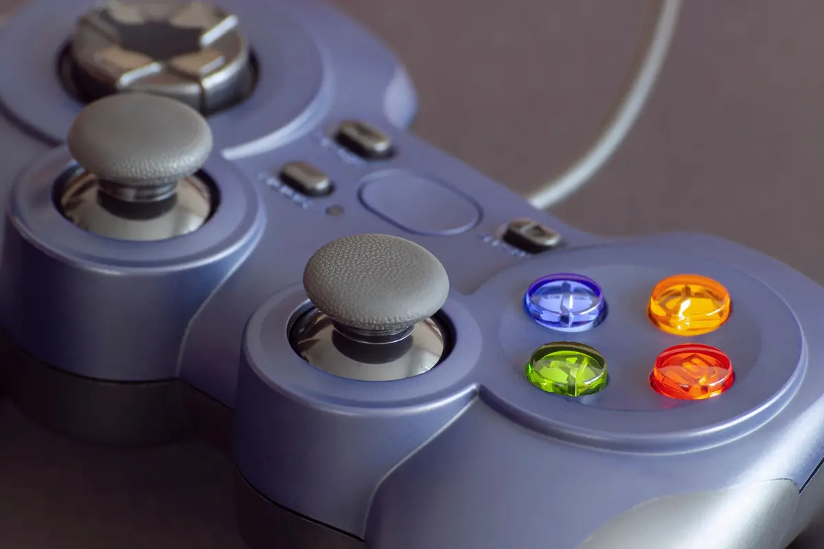 A close-up photograph of a game controller, showing textured analogue sticks, a circular direction pad and four coloured face buttons against a dark background