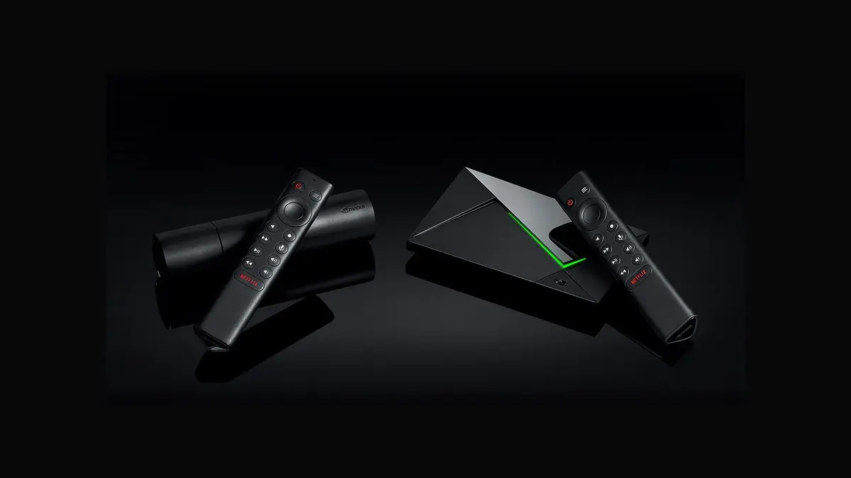 Two black Nvidia Shield TV devices, a tube model and a Shield TV Pro, with their remotes on a glossy black surface