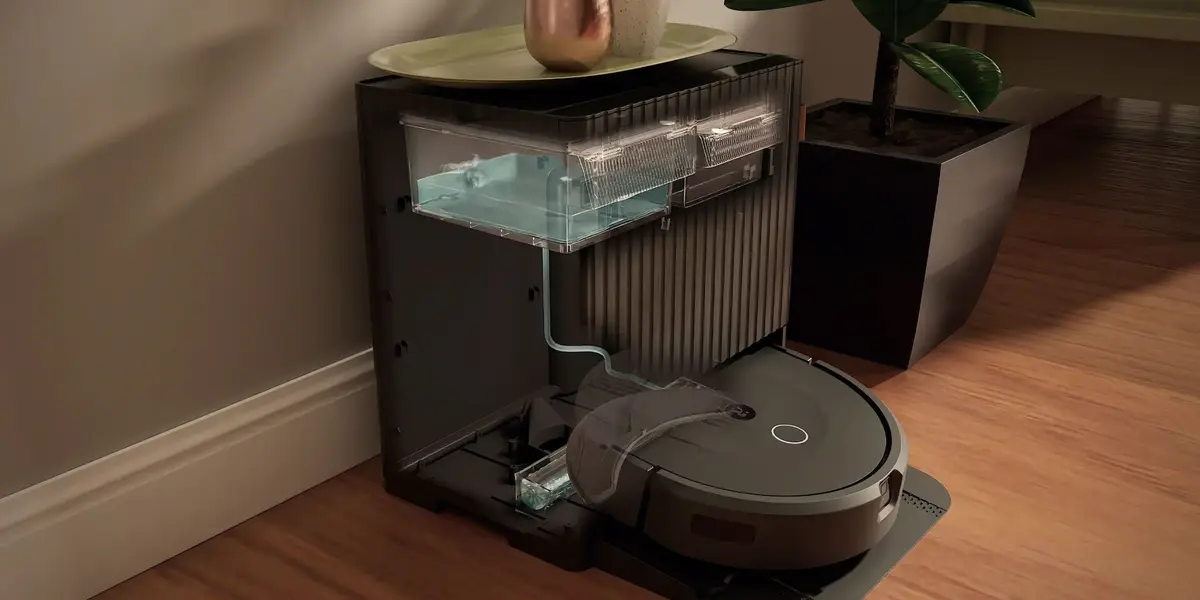 Supplied lifestyle image showing the iRobot Roomba Max 875 Combo robot vacuum beside its AutoWash dock on a wooden floor.
