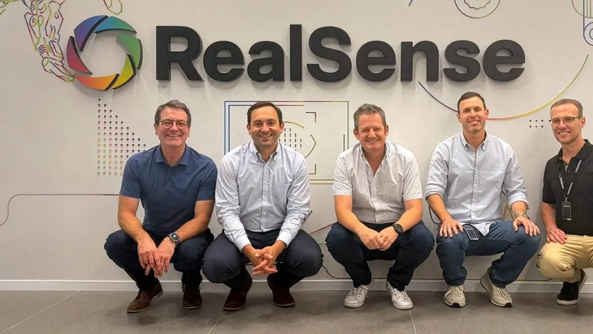 The RealSense wordmark and its multicoloured aperture mark on the company's office wall, with five members of staff crouching in front of it