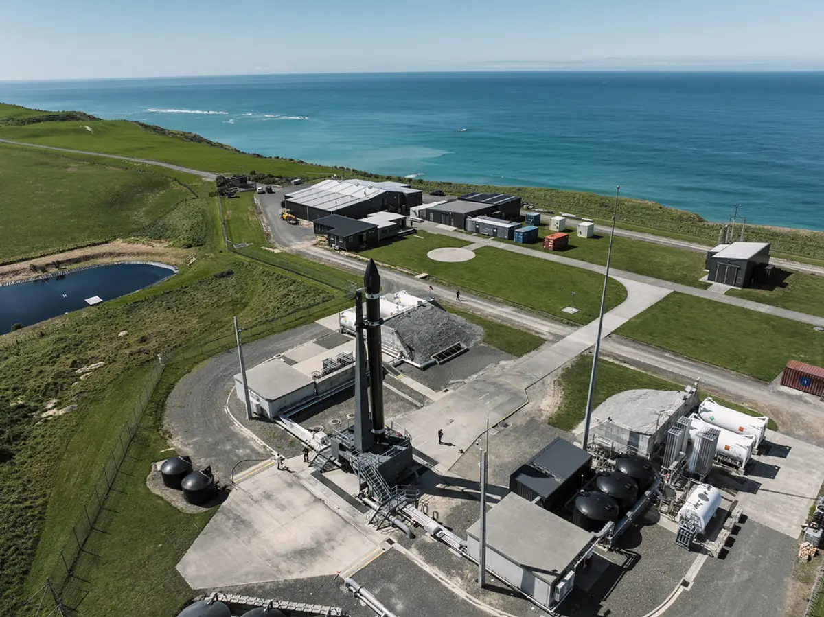 An aerial view of Electron standing on its launch pad at Rocket Lab's Launch Complex 1 on New Zealand's Mahia Peninsula, with the Pacific Ocean behind it