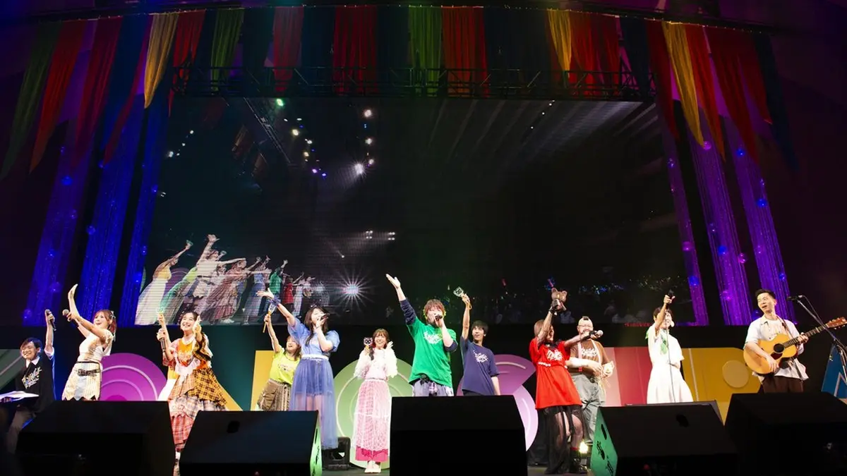 The KonoSuba voice cast on stage at the tenth-anniversary event Colorful, lined up before an illuminated backdrop of multicoloured drapes