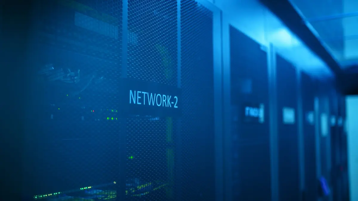 Blue-lit server racks in a data centre, one cabinet labelled NETWORK-2, with rows of network equipment receding into the distance