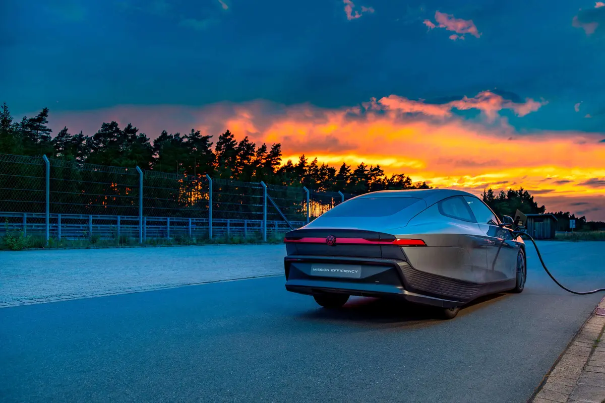 Volkswagen's Mission Efficiency concept car charging at dusk under an orange sunset sky, with the badge and MISSION EFFICIENCY plate visible on the rear