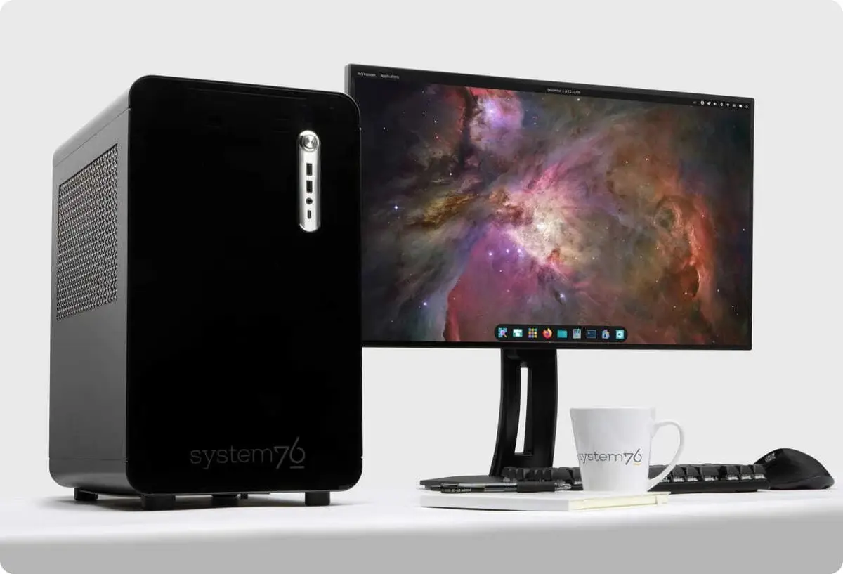 Supplied System76 product photograph showing a black Thelio desktop beside a monitor, keyboard, mouse and coffee mug.