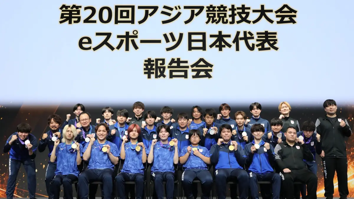 Japan's esports delegation photographed at their Asian Games report event, players in blue national tracksuits holding gold, silver and bronze medals beneath a banner reading 20th Asian Games esports Japan national team report
