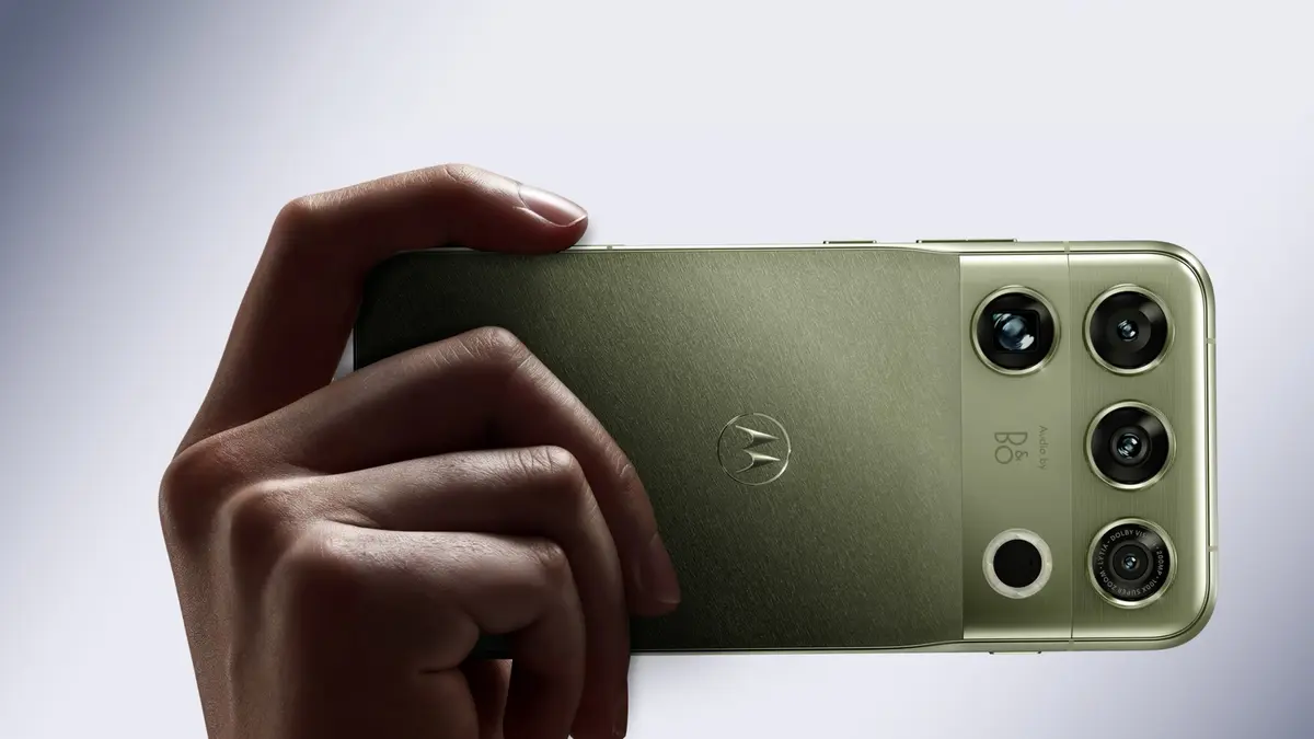 Motorola’s press image for the Signature 27: a hand holding the phone in its olive finish, showing the camera housing marked Audio by B&O and Dolby Vision next to the Motorola batwing logo on the back