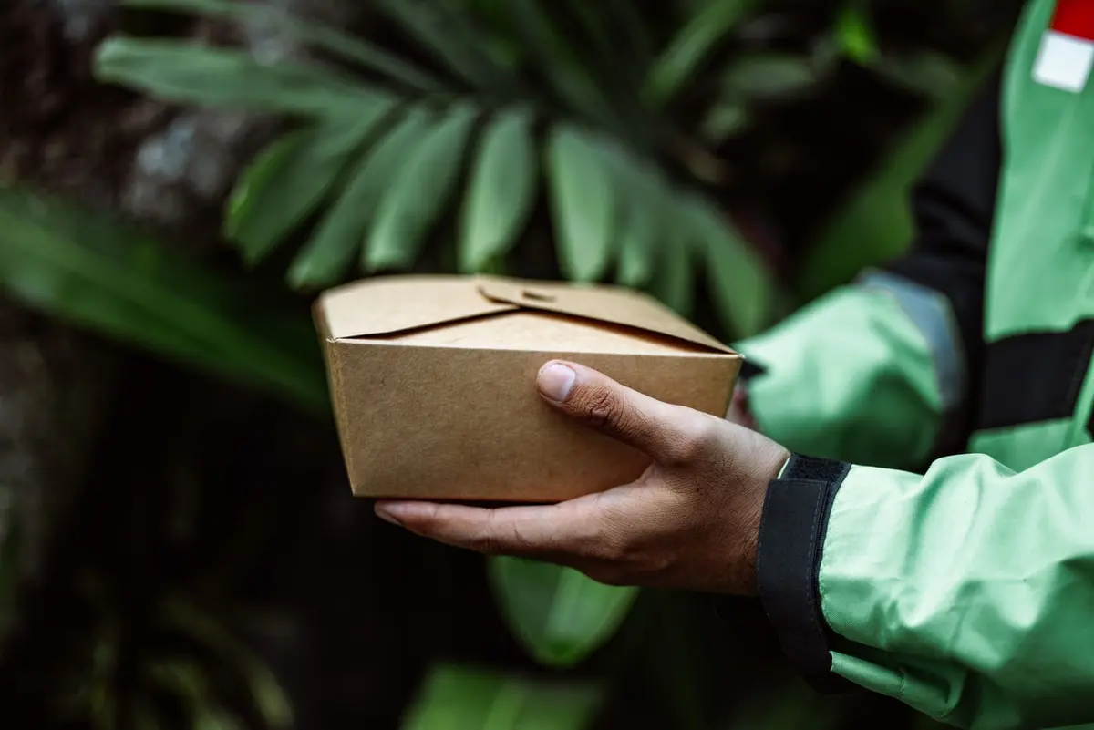 A delivery courier carrying a stack of takeaway food boxes
