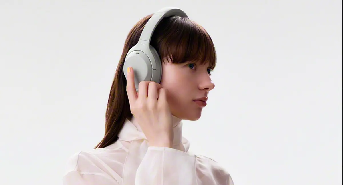 Official Sony product image of a woman wearing the light-grey WH-1000XM4C over-ear noise-cancelling headphones and touching the ear-cup control.