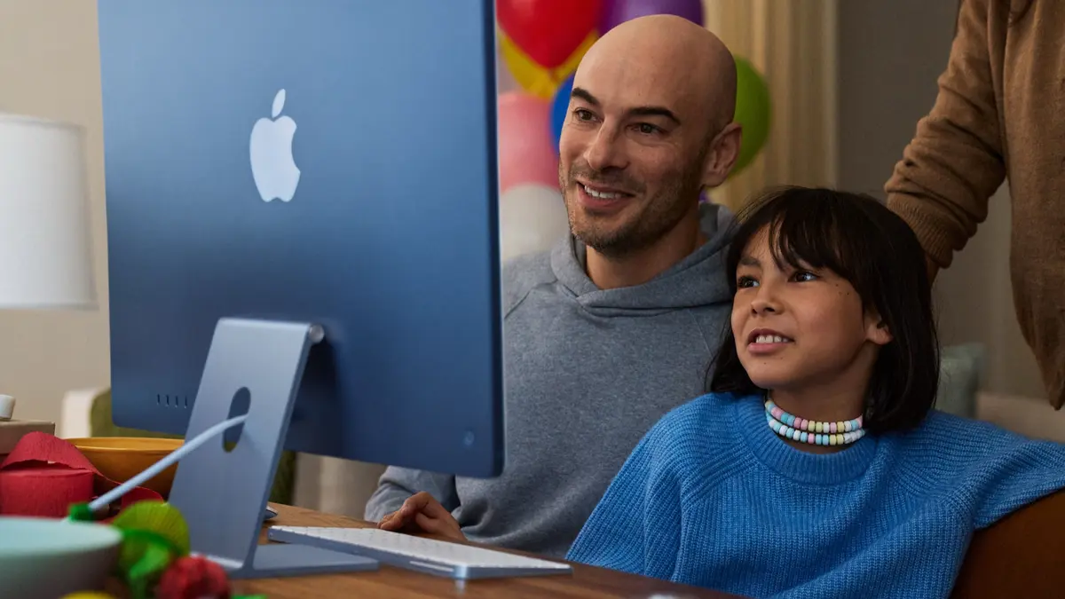 A parent and a child looking at a blue Apple desktop computer together at home