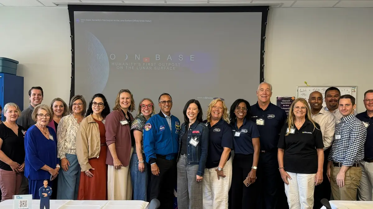 About twenty NASA State Hub project leaders and agency, state and federal partners stand in a group for a photograph in a meeting room, several in NASA-branded shirts and jackets, in front of a projector screen showing a NASA presentation slide.