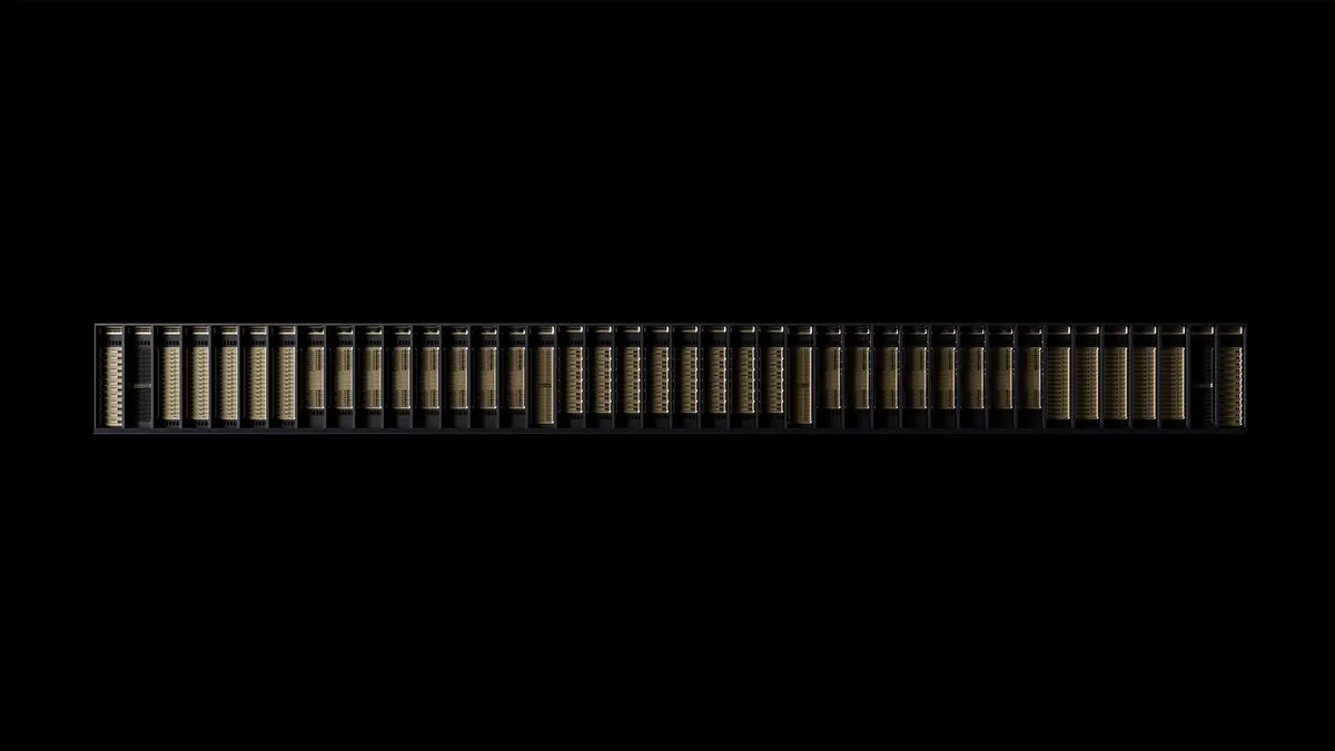 A rack-scale AI system seen head-on as one long row of gold-lit GPU compute trays mounted side by side, set against a black background.