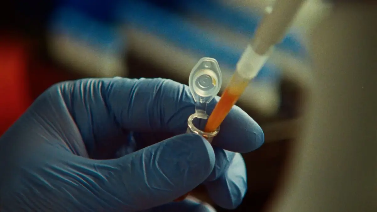 A gloved hand holding a microcentrifuge tube of amber liquid in a laboratory, used as the hero image for a story about an Anthropic lab discovery.