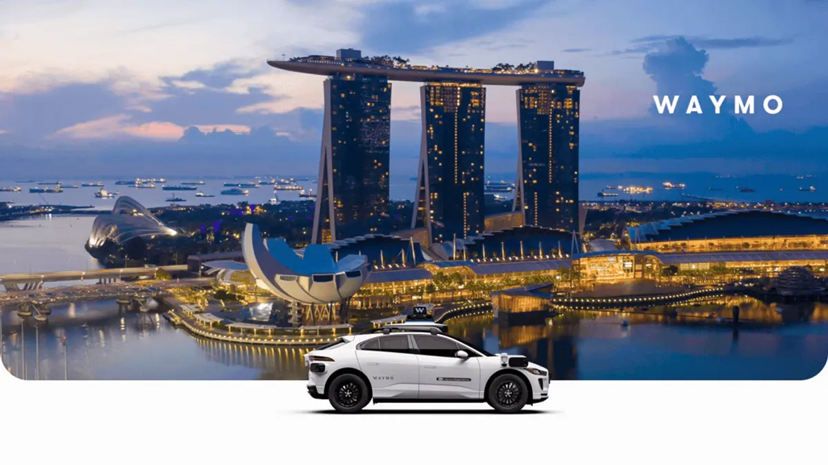 A white Waymo Jaguar I-PACE with a roof-mounted sensor pod in front of Singapore's Marina Bay skyline at dusk