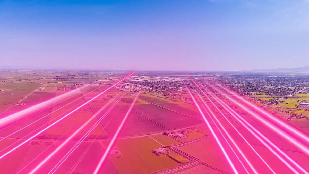 Bright magenta beams of light streaking low across green farmland towards a horizon of fields and low buildings under a blue sky.