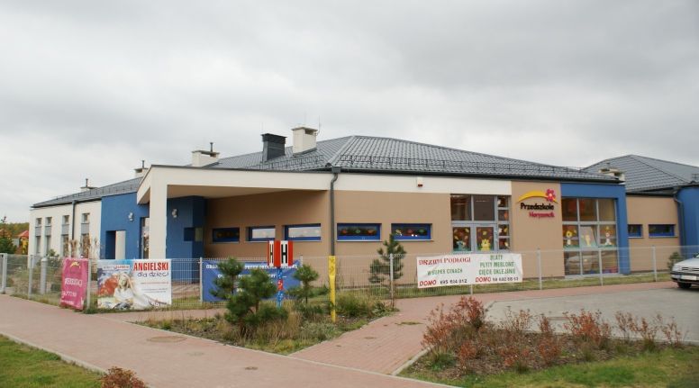 Nowoczesny beżowo-niebieski budynek przedszkola z szyldem „Przedszkole Wesołek”.