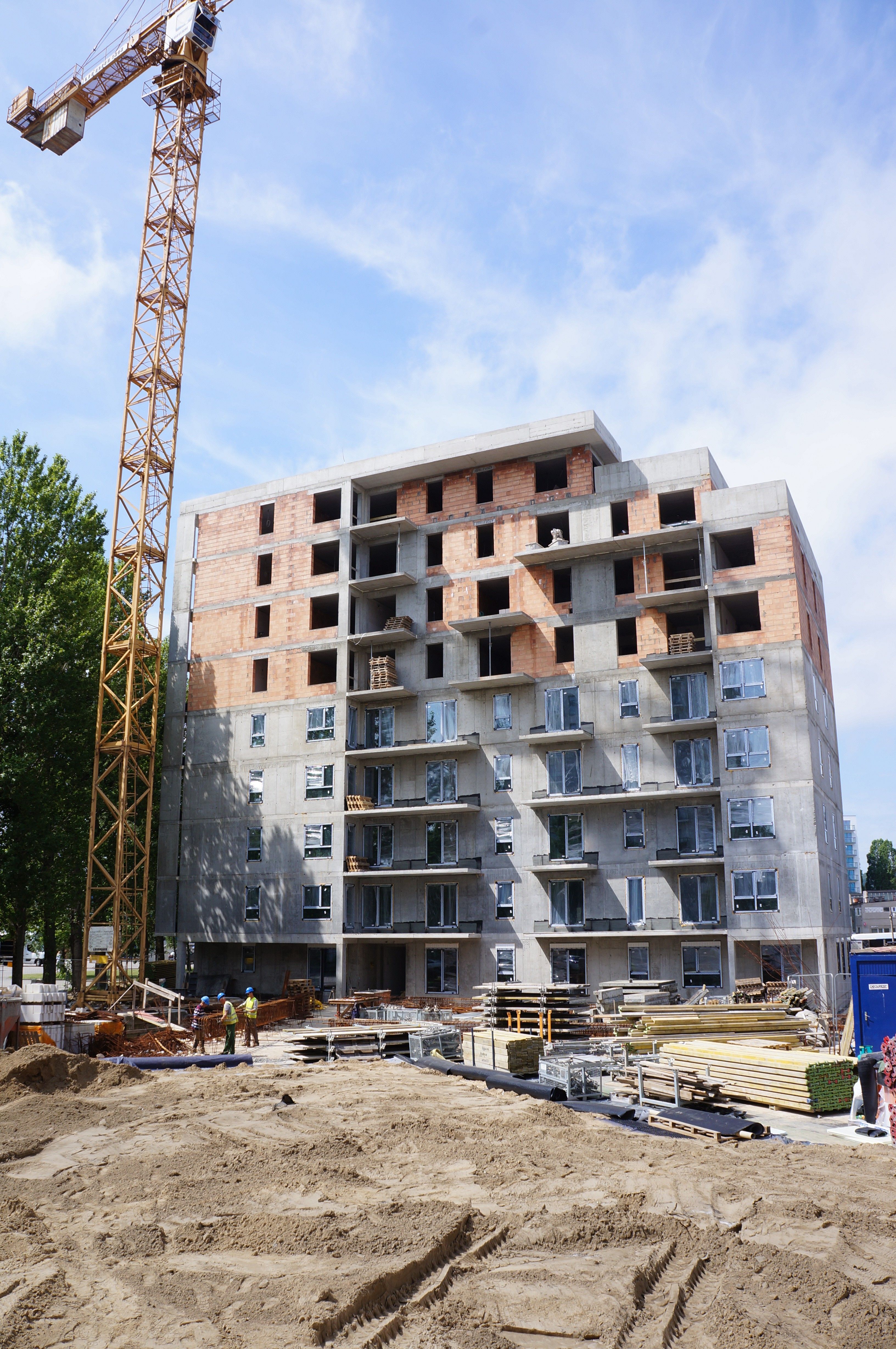 Construction site with a multi-story building, partially complete with concrete and brick, and a tall yellow crane.