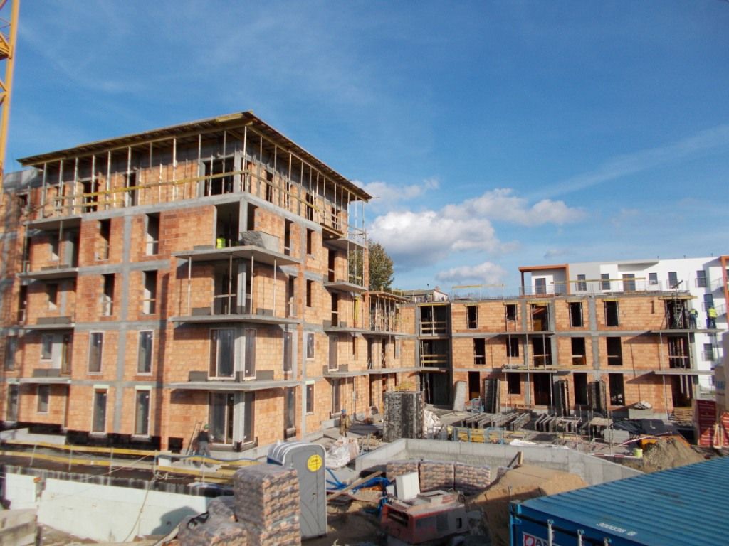 Plac budowy, na którym powstaje kilka wielopiętrowych budynków z cegły i betonu.