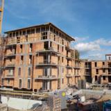 Plac budowy, na którym powstaje kilka wielopiętrowych budynków z cegły i betonu.