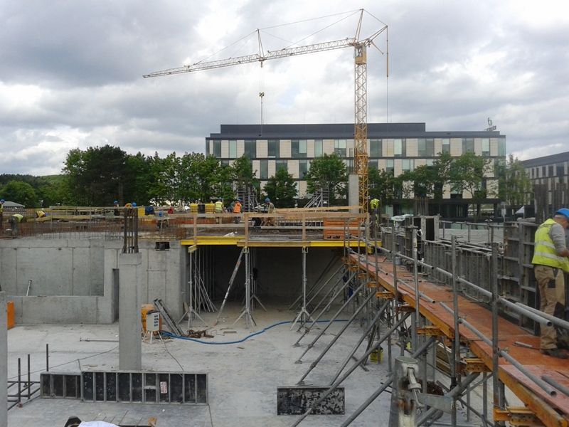 Plac budowy z dźwigiem wieżowym, pracownikami i nowoczesnymi budynkami w tle.