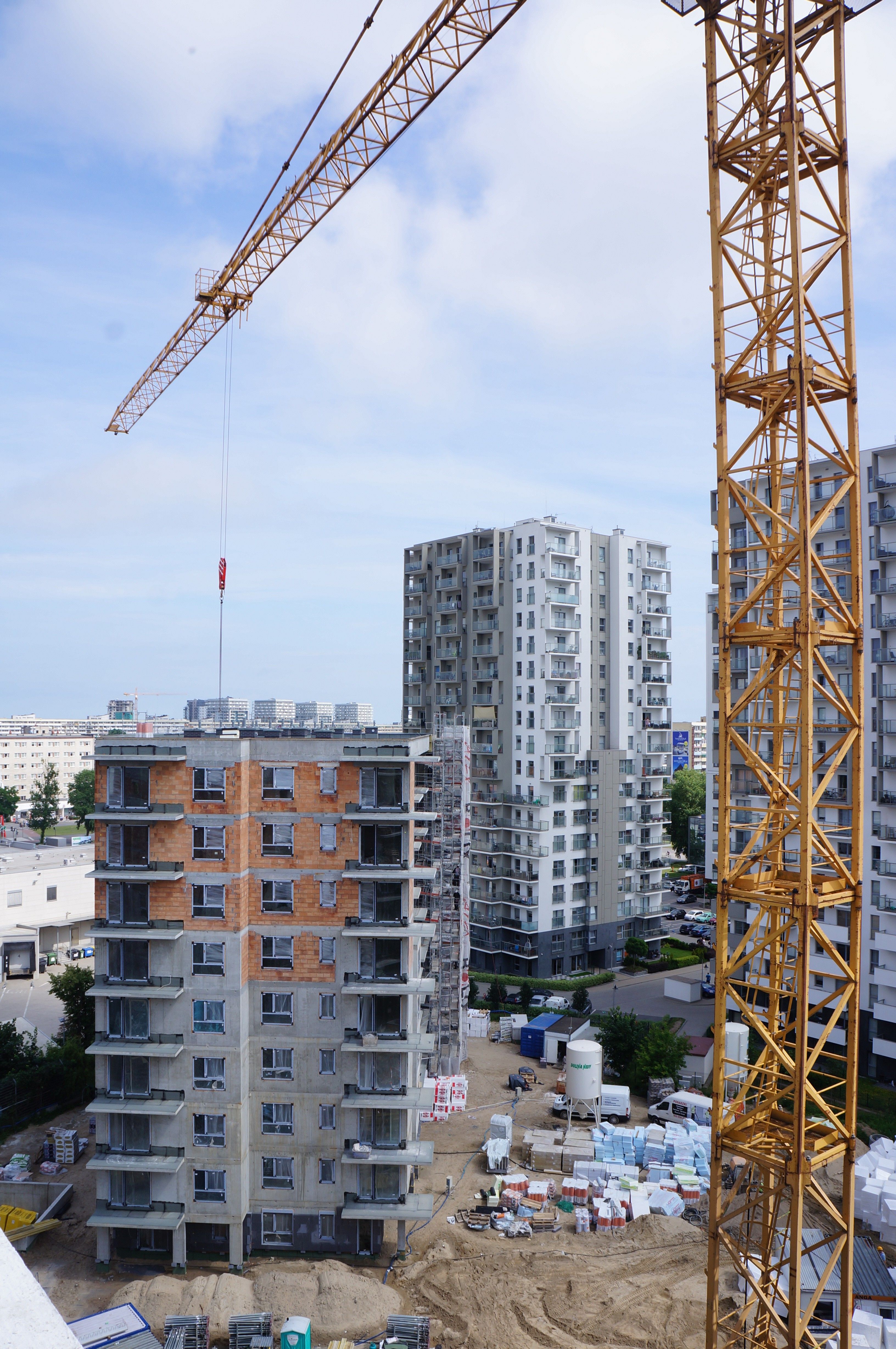 Construction site with a yellow tower crane, a building under construction, and finished apartment blocks.