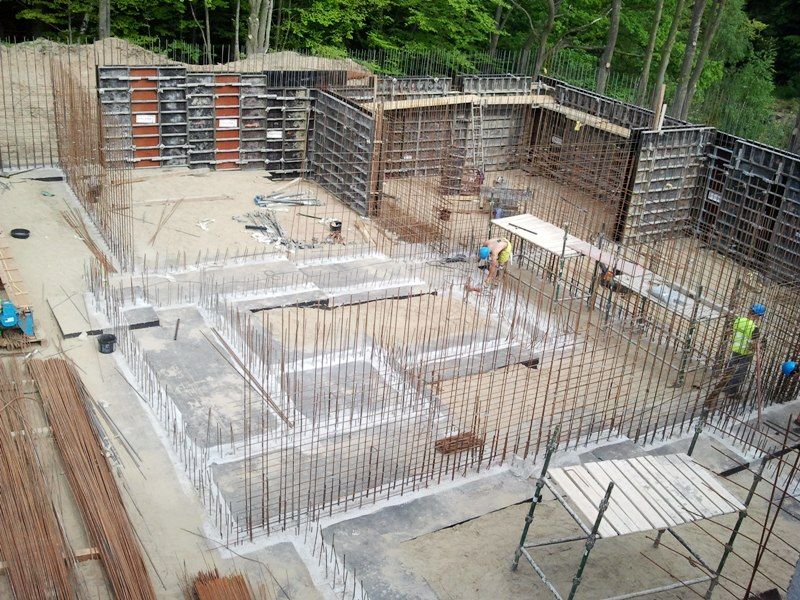 Budowa fundamentów i konstrukcji ścian z użyciem dużej ilości prętów zbrojeniowych, szalunków betonowych i pracowników w dużym dole.