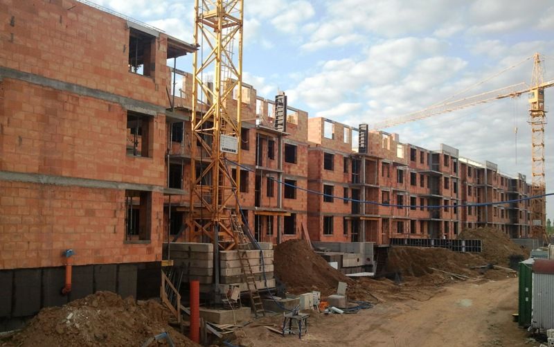 Wielopiętrowy budynek z czerwonej cegły w budowie, wyposażony w dwa dźwigi wieżowe.