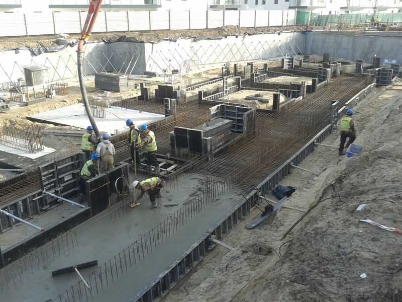 Robotnicy budowlani wylewają beton na fundamenty budynku na placu budowy.